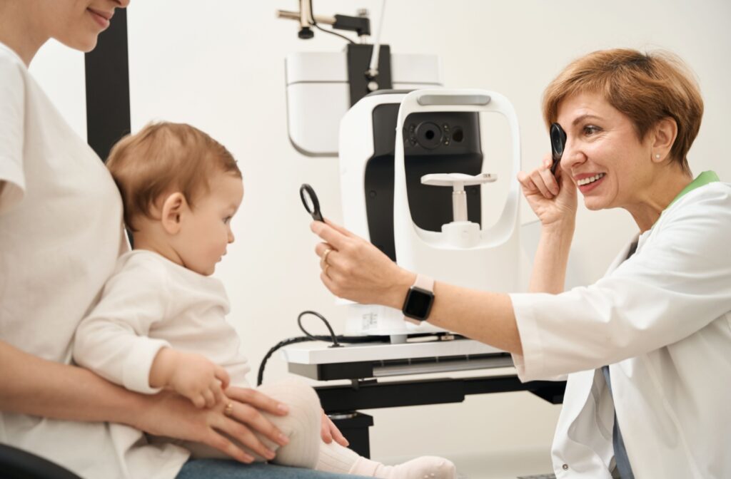 A baby sitting in his mom's lap undergoing an eye exam with a friendly, smiling optician.