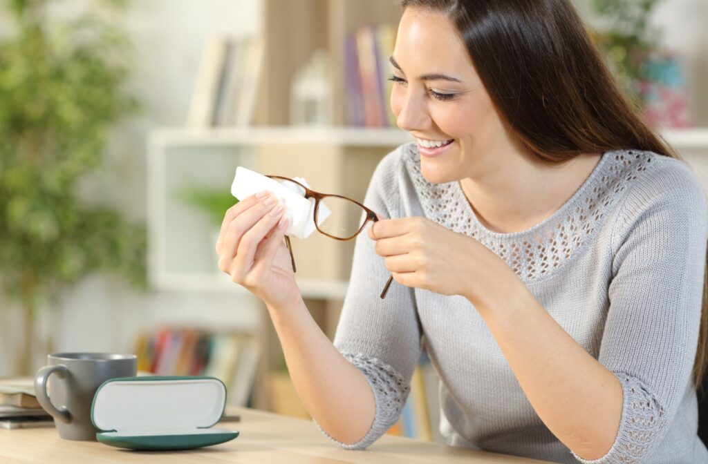 A young woman smiles as she cleans her eyeglasses with a microfiber cloth, ready to put them away in a protective case