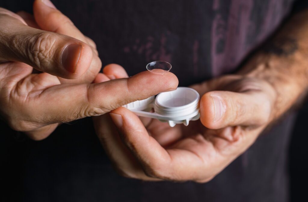 An individual holds a contact lens case in one hand while balancing a single contact lens on an index finger.