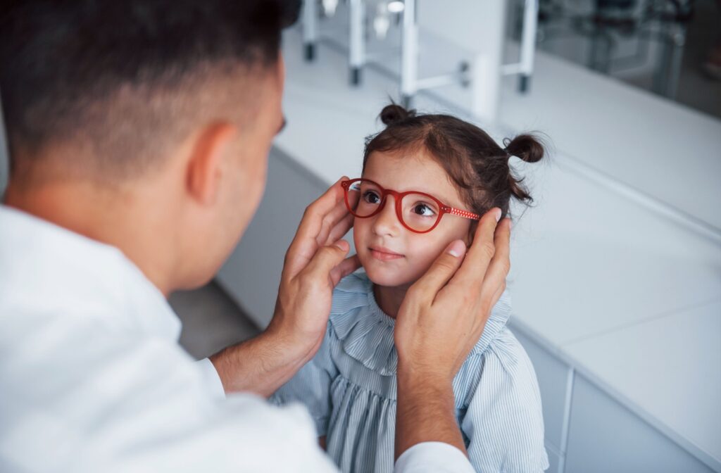 An eye doctor helps a young girl pick out a pair of red glasses.